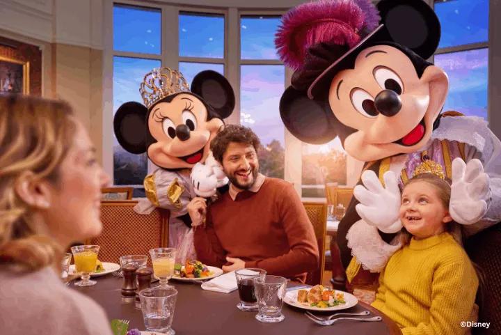 Mickey Mouse and Minnie Mouse in royal attire greeting a family dining at the Royal Banquet inside Disneyland Hotel in Disneyland Paris