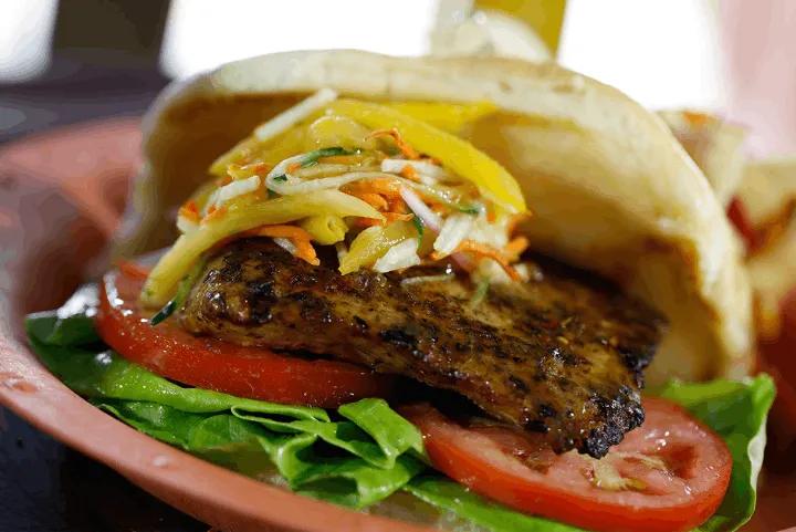Grilled jerk mahi mahi sandwich topped with mango slaw, lettuce, and sliced tomatoes