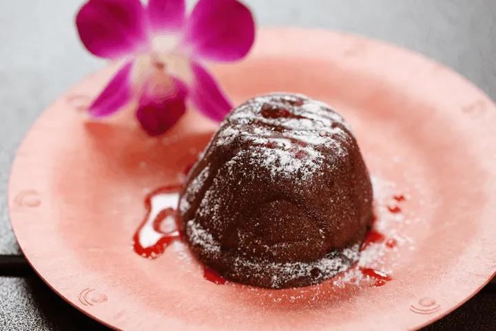 Mini chocolate lava cake dusted with powdered sugar and drizzled with fruit sauce on a pink plate
