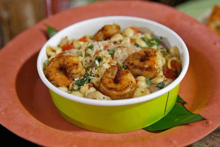 Bowl of shell mac and cheese topped with seared jerk shrimp, herbs, and spices