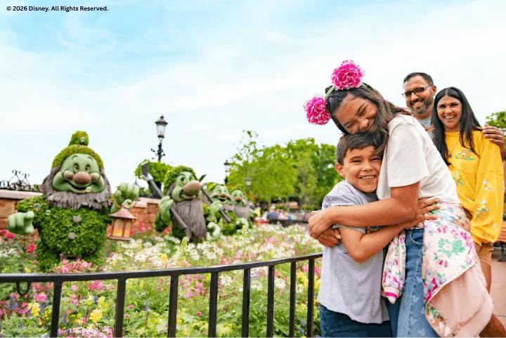 Family hugging in front of Seven Dwarfs topiaries and colorful flowers at EPCOT