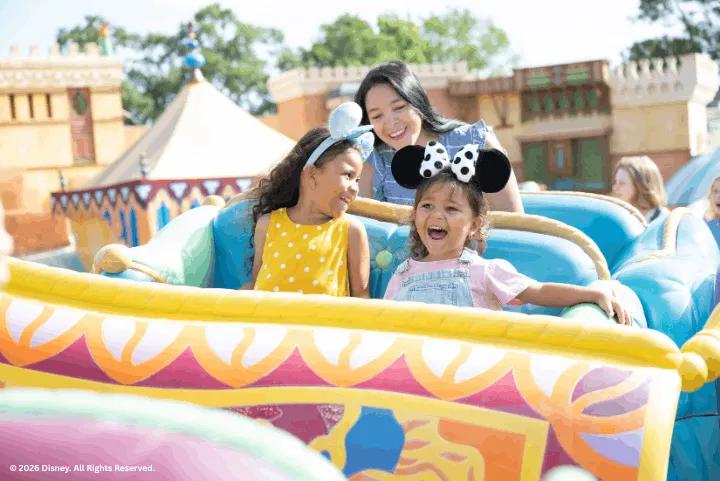 A woman and two young girls in mouse ears smiling on the Magic Carpets of Aladdin ride