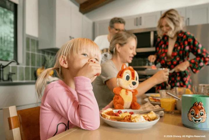 A young girl eating breakfast with her family inside a cabin kitchen featuring Chip and Dale decor