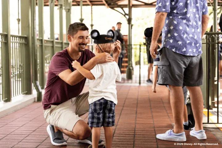 A smiling father adjusting Mickey ears on his young child at a train station platform