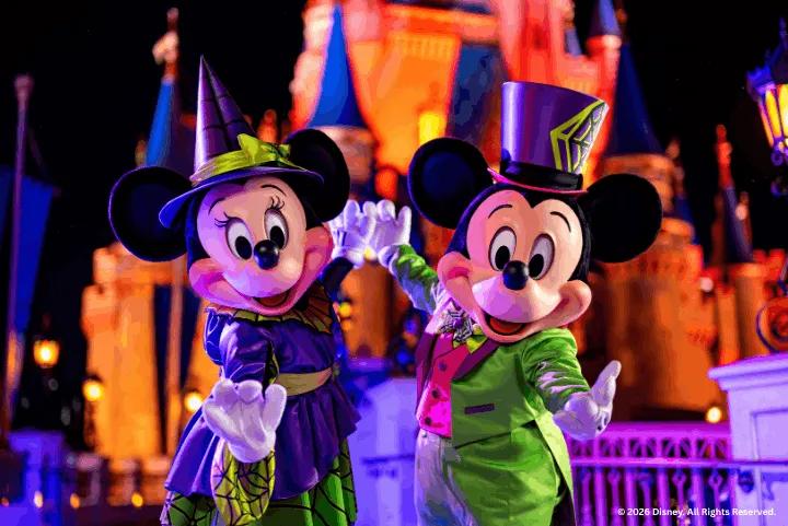 Mickey Mouse and Minnie Mouse wearing Halloween costumes in front of a brightly lit castle