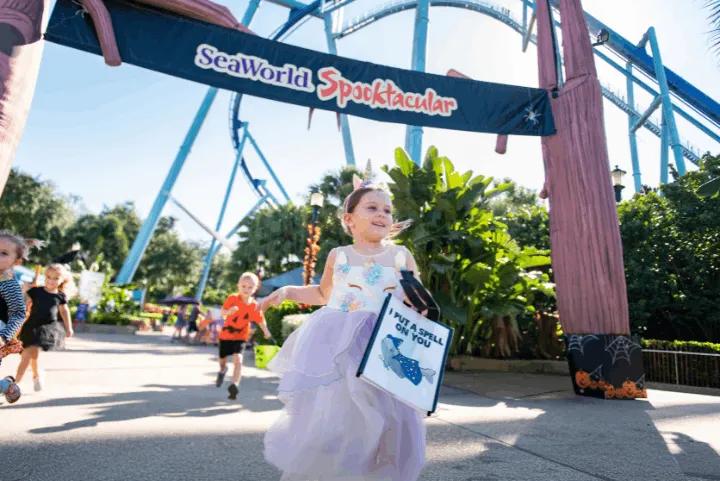 Children in Halloween costumes running with reusable bags under a SeaWorld Spooktacular event sign
