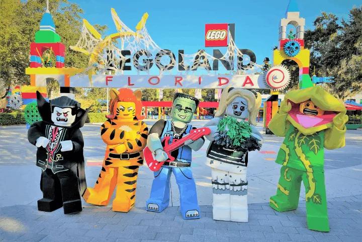 Five LEGO costume characters posing in front of the LEGOLAND Florida entrance decorated for Halloween