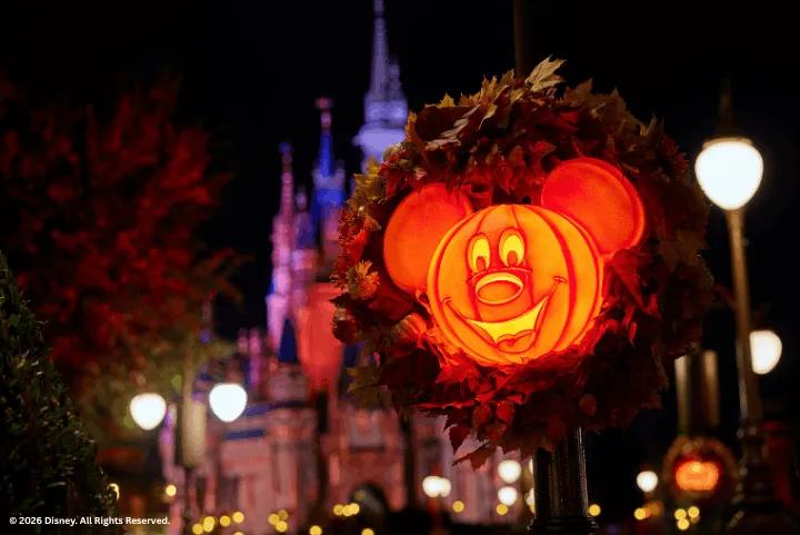 A glowing Mickey Mouse pumpkin wreath on a lamppost with Cinderella Castle in the background