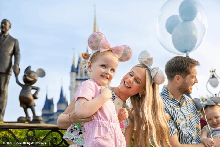 A mother and daughter wearing mouse ears smiling together in front of Cinderella Castle and the Partners Statue at Magic Kingdom