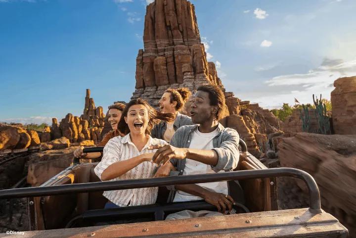 A group of cheerful guests riding a mine train coaster past red rock formations on Big Thunder Mountain