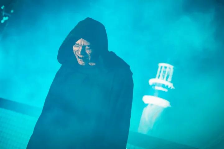 A hooded scareactor with sinister makeup posing in blue fog in front of the SeaWorld lighthouse