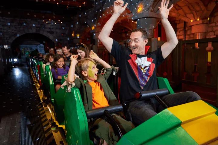 A man and young boy in Halloween costumes riding the Dragon roller coaster at Legoland Windsor