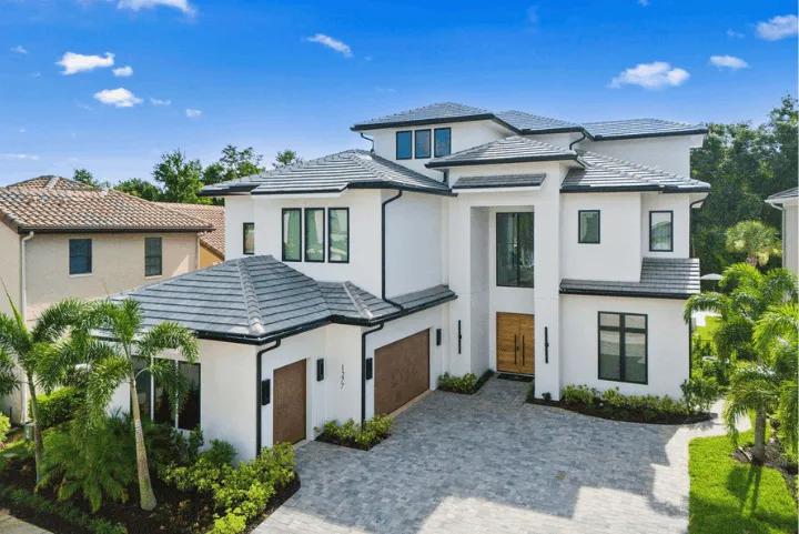 Exterior view of a two-story modern white luxury villa in Orlando with a paved driveway, tile roof, and palm trees