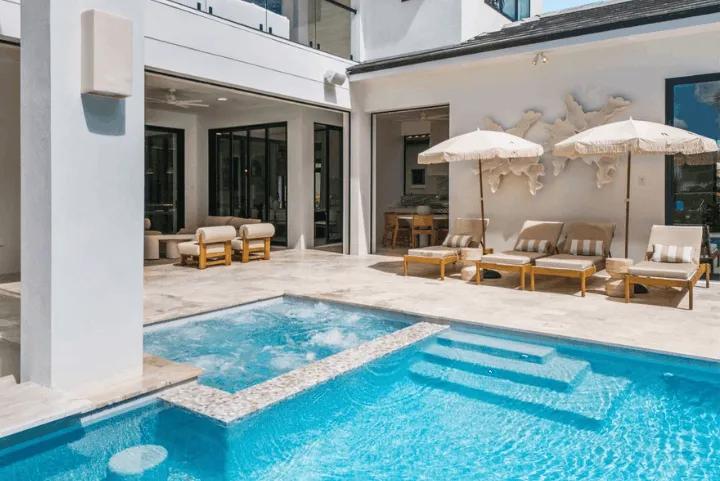 A luxury outdoor patio with a swimming pool, attached hot tub, and lounge chairs with umbrellas