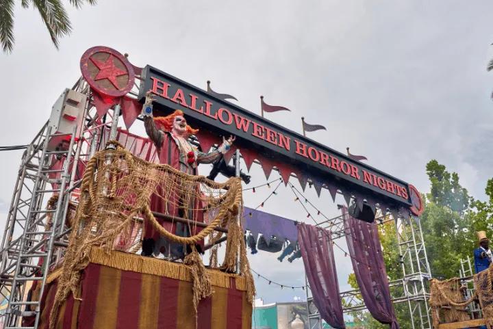Jack the Clown standing atop a carnival platform under a Halloween Horror Nights entrance sign