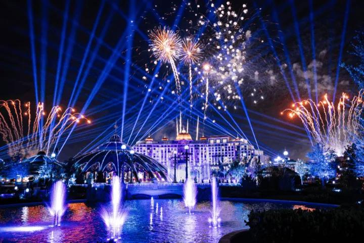Nighttime spectacular featuring fireworks, blue laser lights, and illuminated water fountains in front of a large hotel