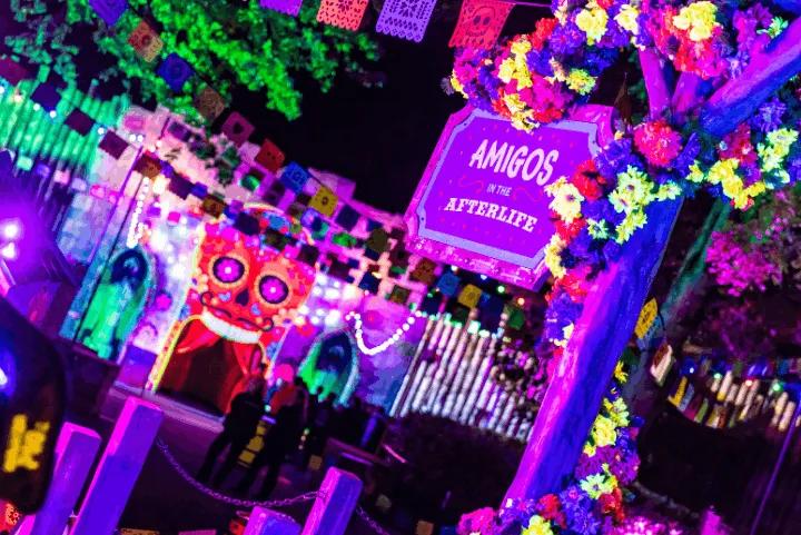 A brightly colored, neon-lit sign and entrance for the Amigos in the Afterlife attraction