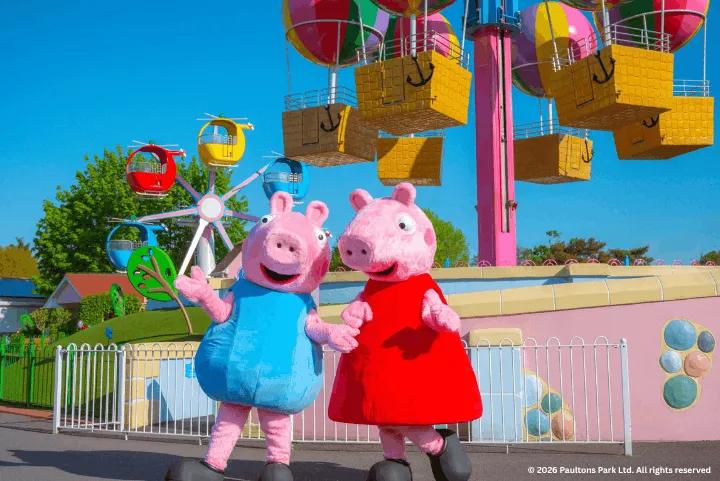 Peppa Pig and George mascots standing in front of colorful rides at Peppa Pig World