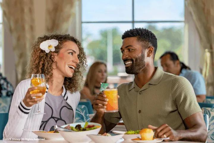 A couple smiling and toasting with tropical drinks while dining at Disney's Caribbean Beach Resort