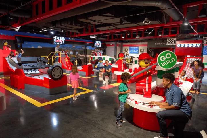 Children and adults building and testing LEGO race cars at the brightly lit LEGO Ferrari Build & Race play area