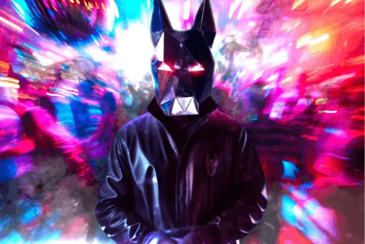 A person wearing a black leather jacket and a geometric dog mask with glowing red eyes, standing in front of vibrant, blurry neon lights