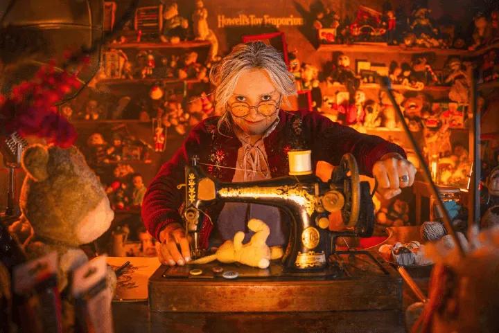 A sinister-looking woman with glasses operating a vintage sewing machine in a dimly lit room filled with dolls and toys