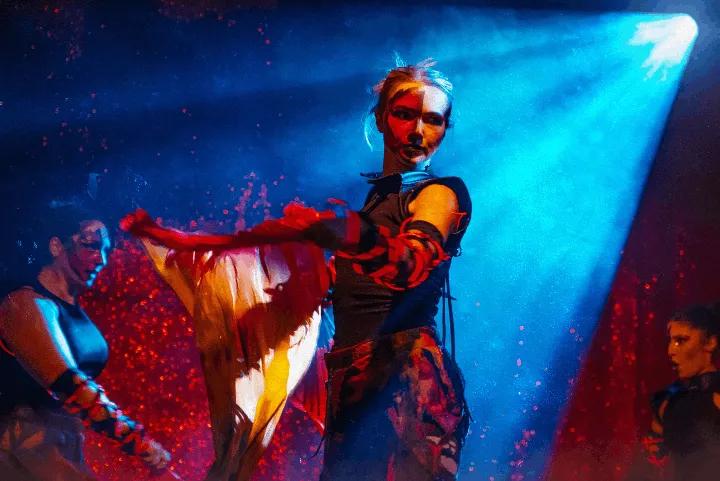 Performers on a stage illuminated by a bright blue spotlight against a sparkly red background