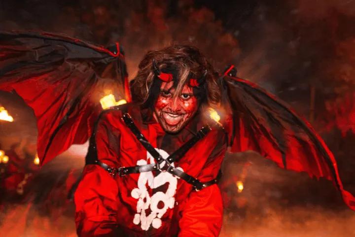 A scare actor dressed as a demon with horns, red face paint, and black wings