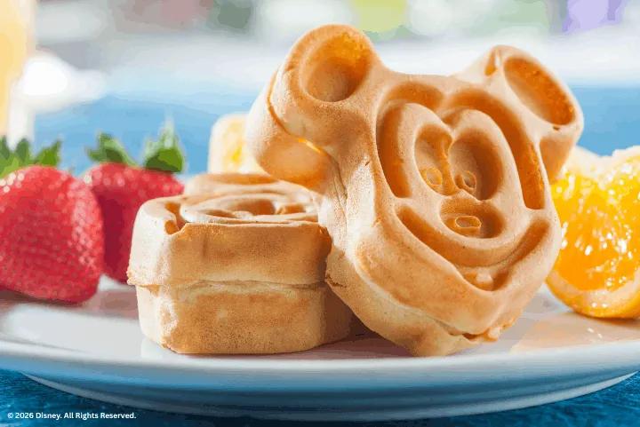 Golden-brown Mickey Mouse shaped waffles on a plate with fresh fruit