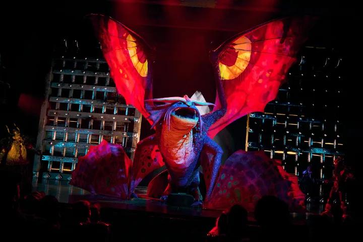 Large animatronic dragon with glowing red wings on a stage during a performance