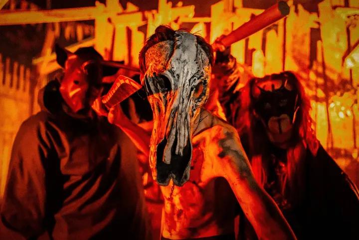 Masked cultists in red lit surroundings holding props in the Burial Grounds scare zone