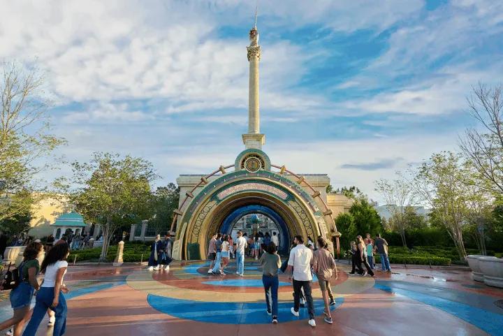 Guests walking through an ornate portal archway beneath a tall column at the entrance to The Wizarding World of Harry Potter - Ministry of Magic