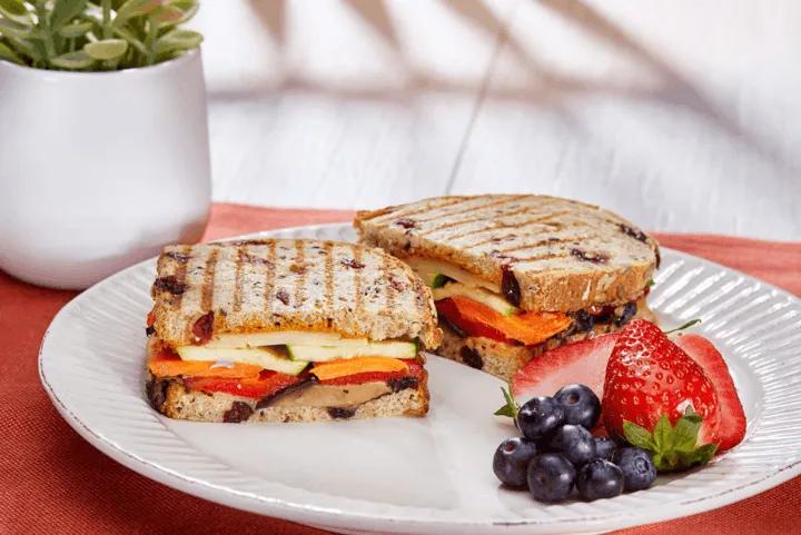 A grilled veggie sandwich served with fresh strawberries and blueberries on a plate at TODAY Cafe