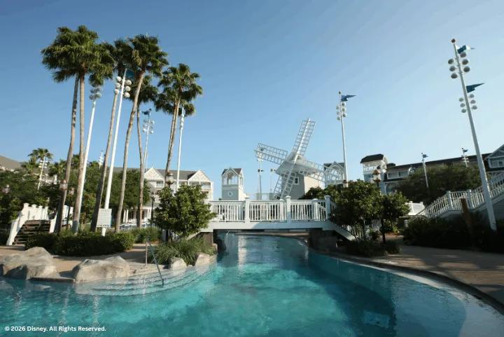 A sandy bottom pool area with a white windmill bridge and palm trees