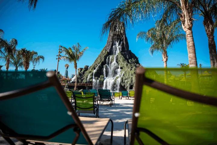 Green lounge chairs framed in front of a large tropical volcano with cascading waterfalls