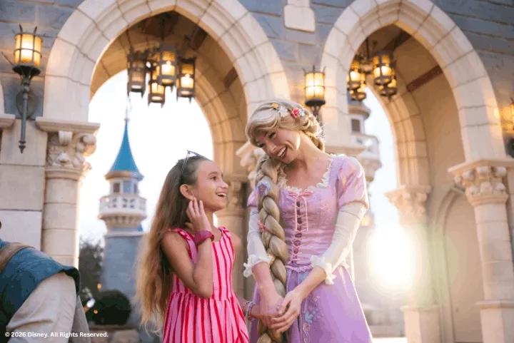 A young girl in a pink dress smiling while interacting with Rapunzel under stone castle arches