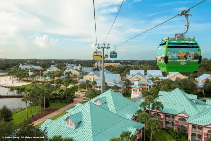 A green Skyliner gondola gliding above colorful resort buildings and palm trees