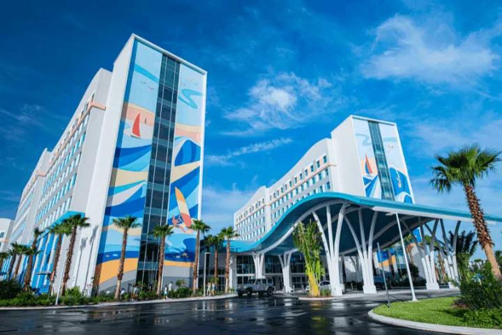 Exterior view of a surf-themed resort hotel with blue ocean murals and a curved portico under a sunny sky