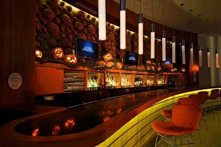 The Pumpkin Lord Bar at Swizzle Lounge in Universal Cabana Bay Beach Resort, featuring carved jack-o'-lanterns decorating the back bar wall