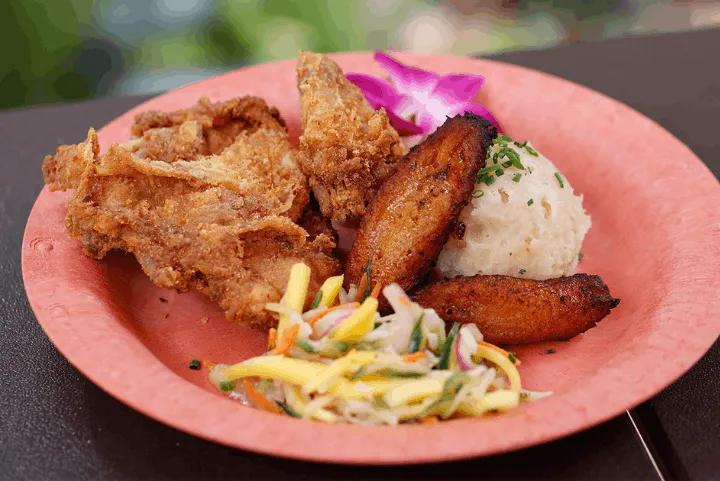 Plate of coconut-crusted fried chicken served with plantains, rice, and slaw