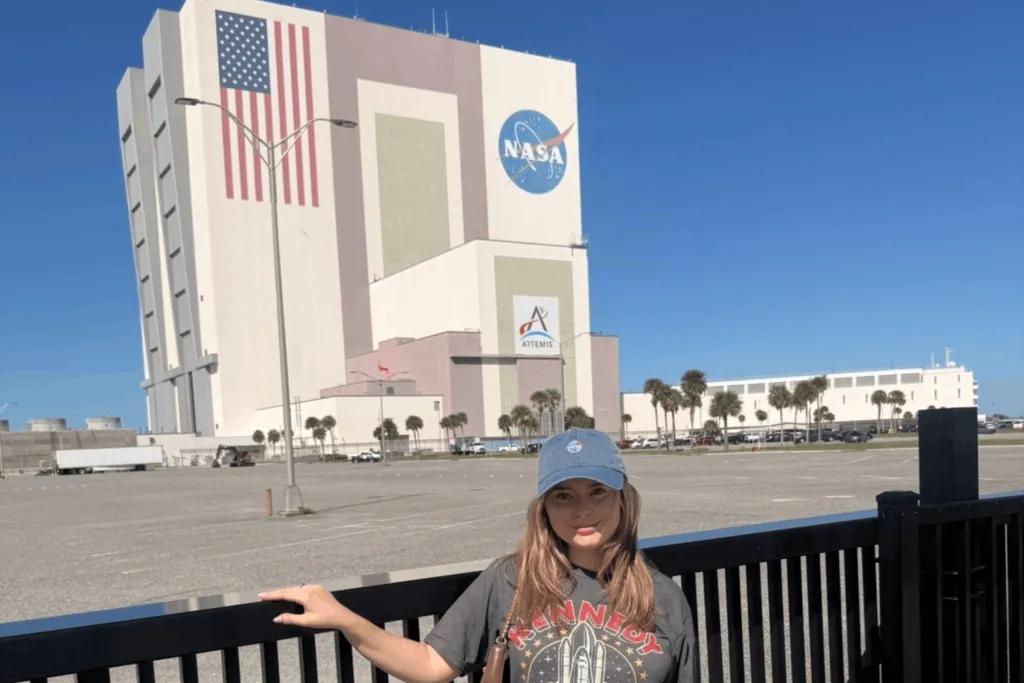 Freya stood in front of huge building, the Vehicle Assembly Building, with NASA sign on and huge american flag