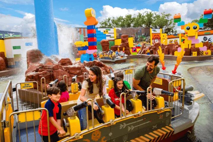 A family smiling on a LEGO-themed water ride while spraying water cannons at a theme park