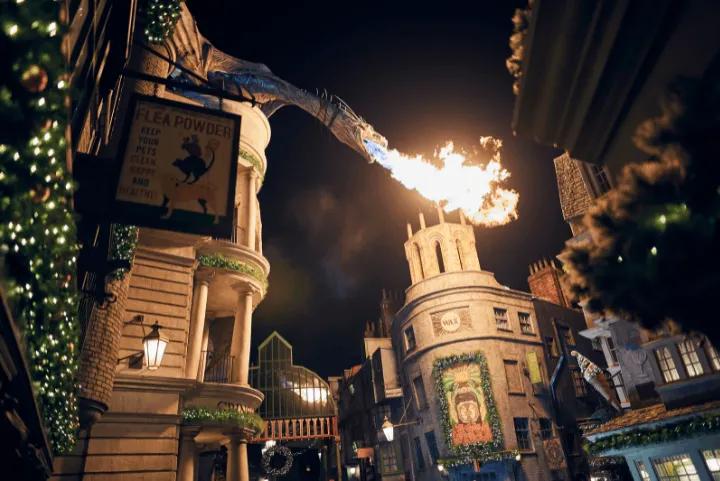 A dragon atop a building breathes fire over a street decorated for Christmas at night