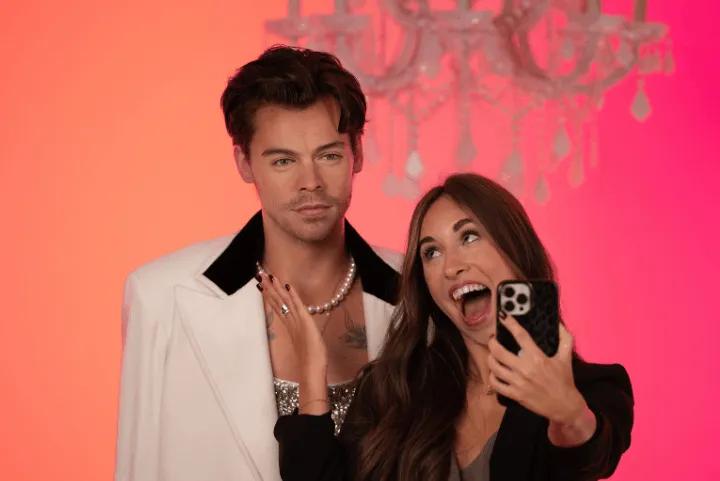 Alt Text: A woman taking a selfie with a wax figure of Harry Styles