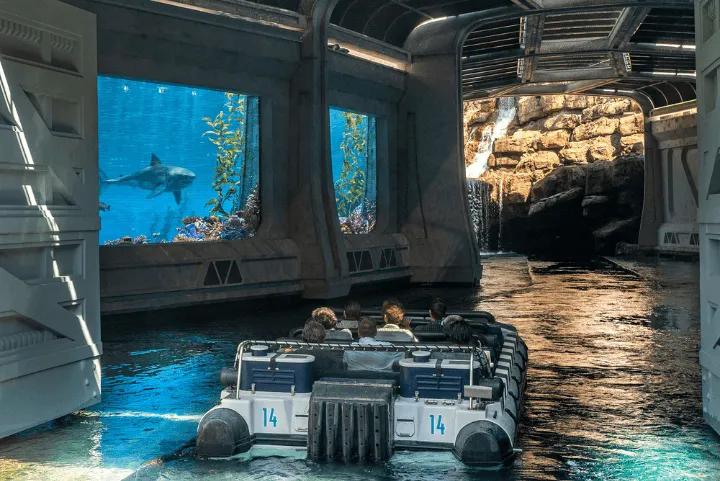 Guests in a ride boat passing a large screen displaying a shark on Jurassic World - The Ride