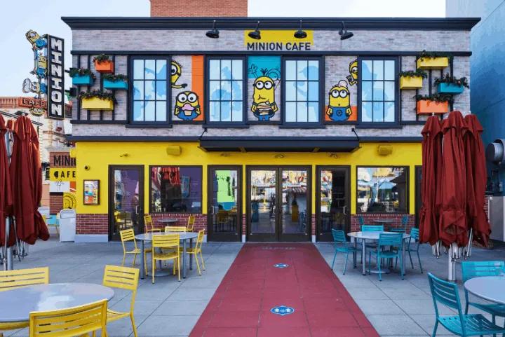 The bright yellow exterior of the Minion Cafe featuring window graphics of Minions and an outdoor patio seating area