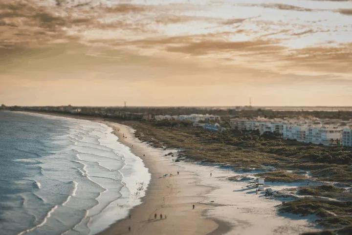 Aerial view of a sandy beach coastline with waves and distant buildings