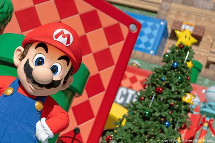 Mario poses in front of a decorated Christmas tree topped with a yellow Super Star