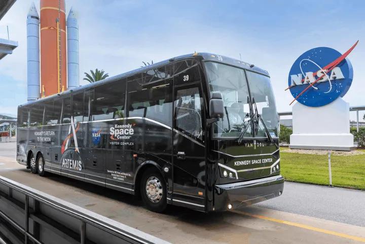 A black Artemis-themed Kennedy Space Center tour bus parked outside the visitor complex near the iconic NASA logo sign
