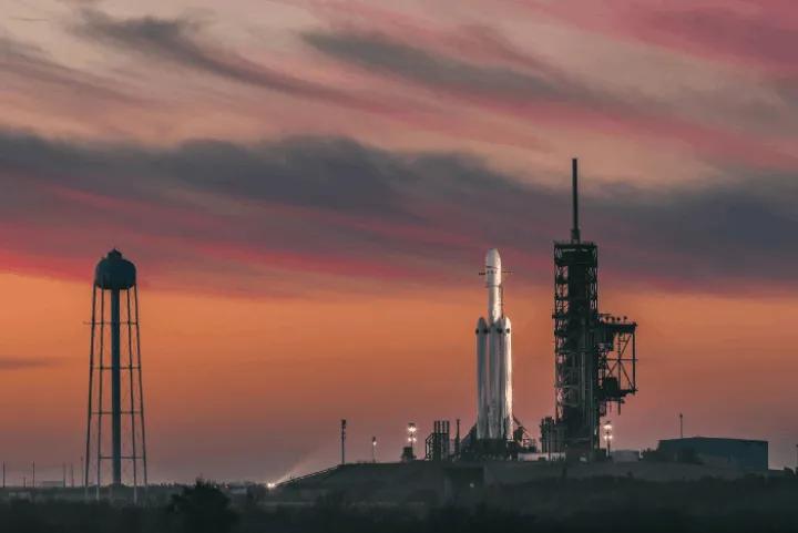 A SpaceX Falcon Heavy rocket standing on a launch pad at sunset